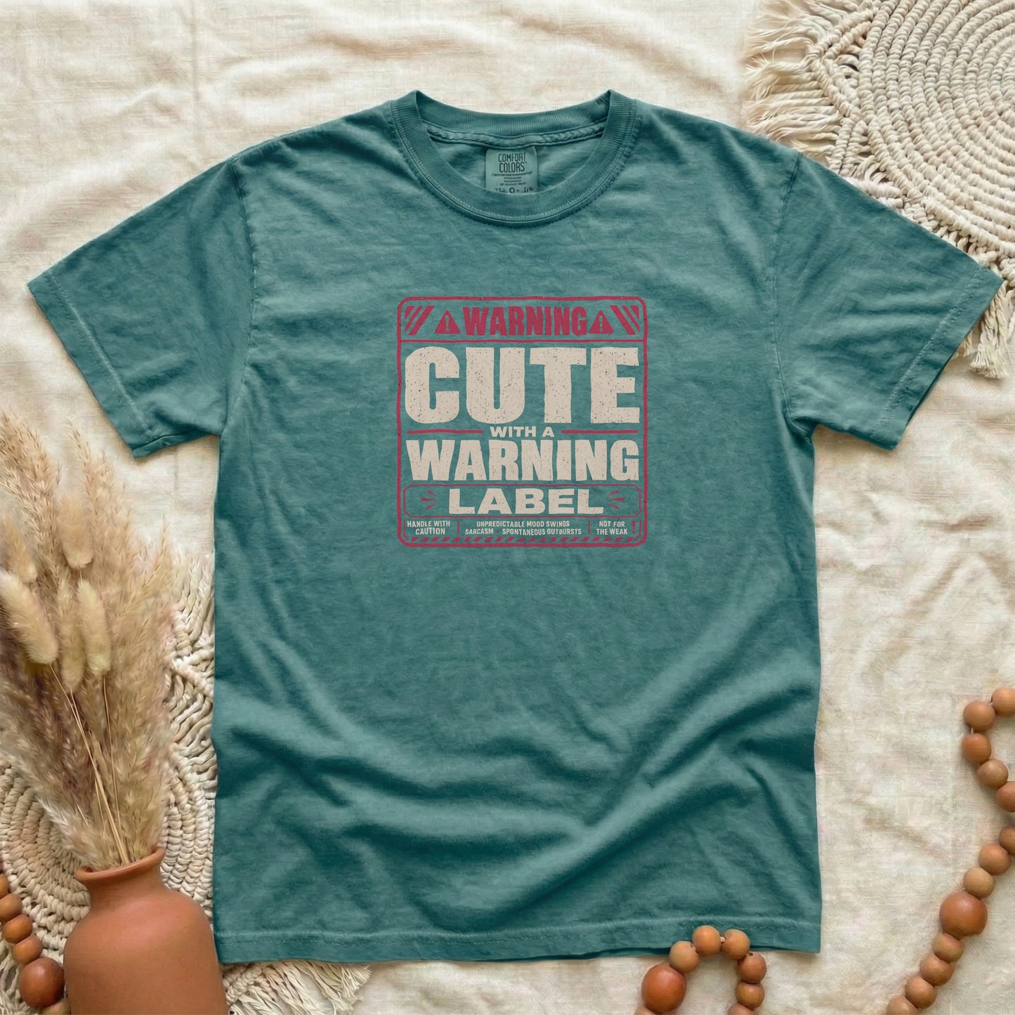 Blue Spruce garment-dyed cotton tee printed with "Cute With A Warning Label".