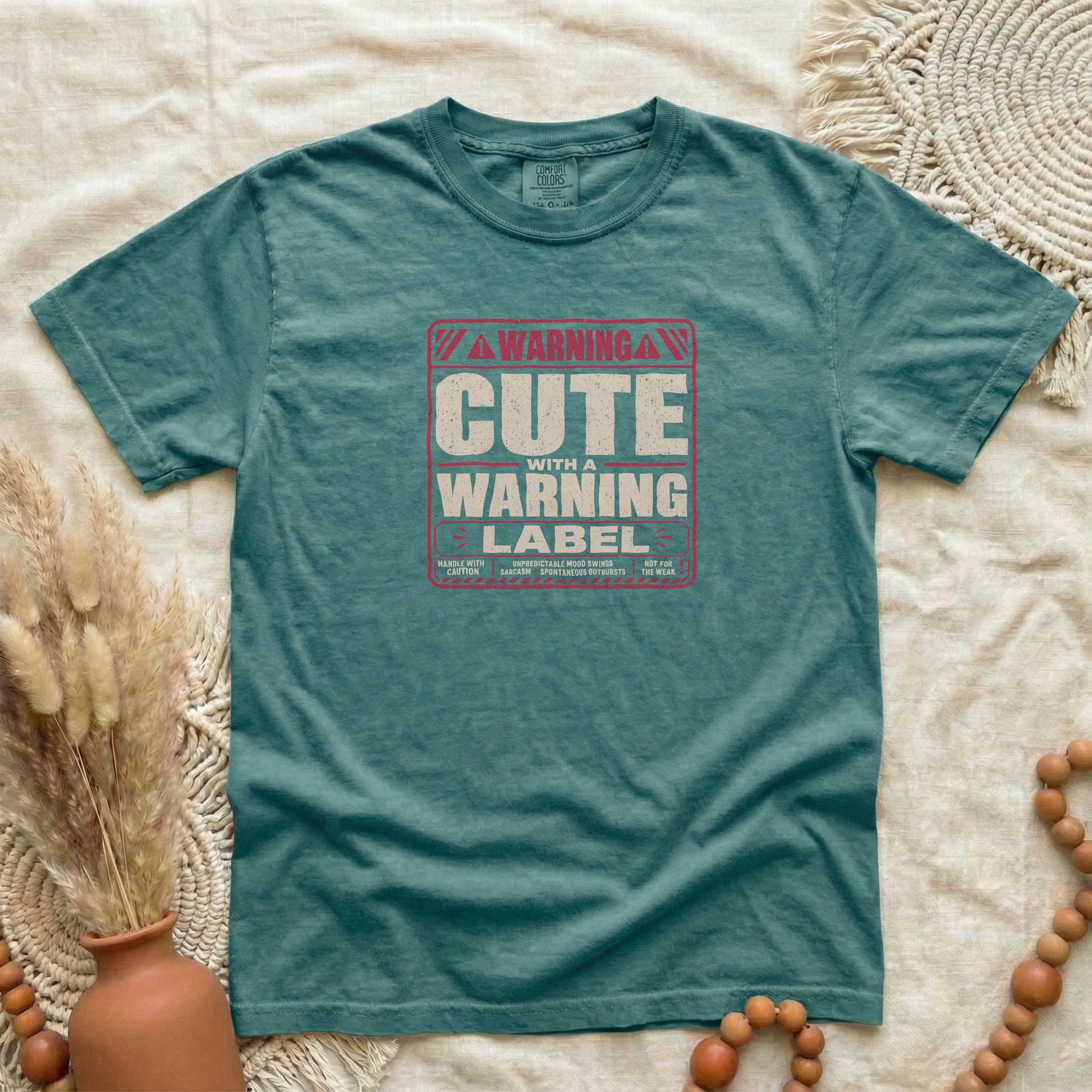 Blue Spruce garment-dyed cotton tee printed with "Cute With A Warning Label".