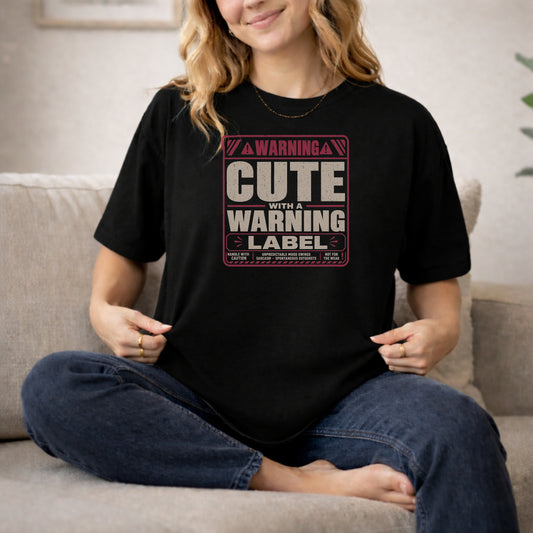 Black garment-dyed cotton tee printed with "Cute With A Warning Label".